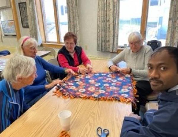 Nicole Duhamel and Josh Lussier (sisters) fold a prayer blanket while Nan, District Deputy Rose Pelchuck and Fr. Thomas Aquinas look on.